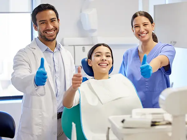 Woman smiling and giving a thumbs up in the dental chair with hygienist and dentist 