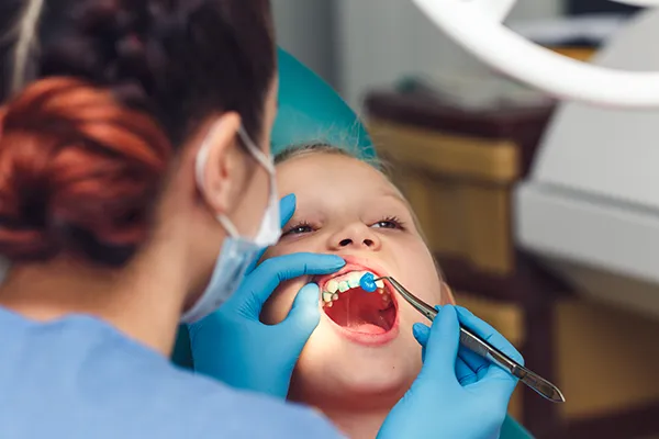 Girl patiently keeping her mouth open while her dentist applies fluoride solution to her teeth